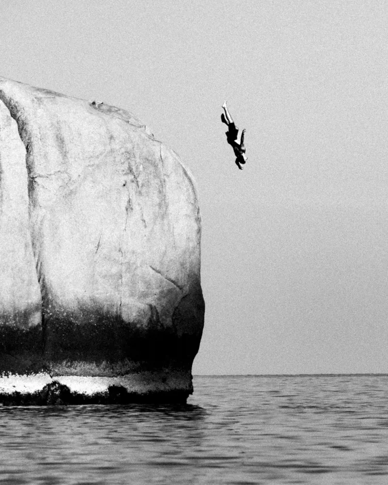 A figure dropping from a limestone boulder into open water, Koh Tao, Thailand