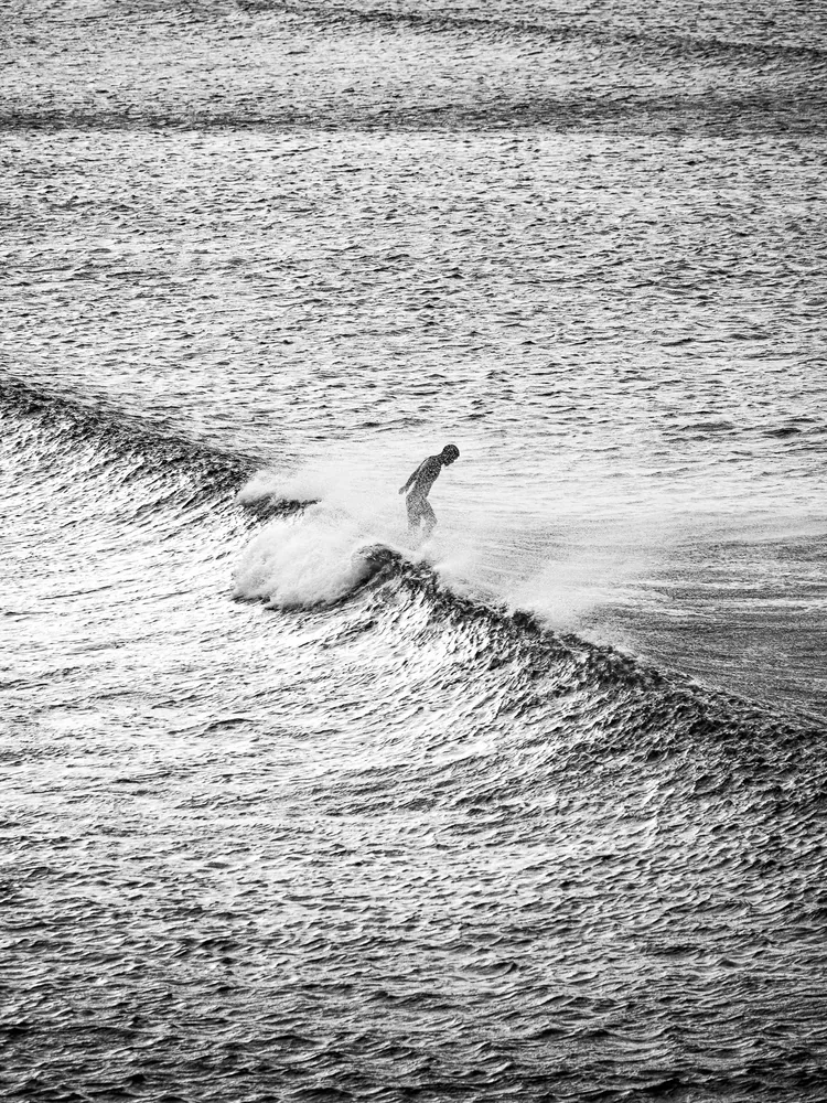 A lone surfer crossing a wide black-and-white sea, San Sebastián, Spain